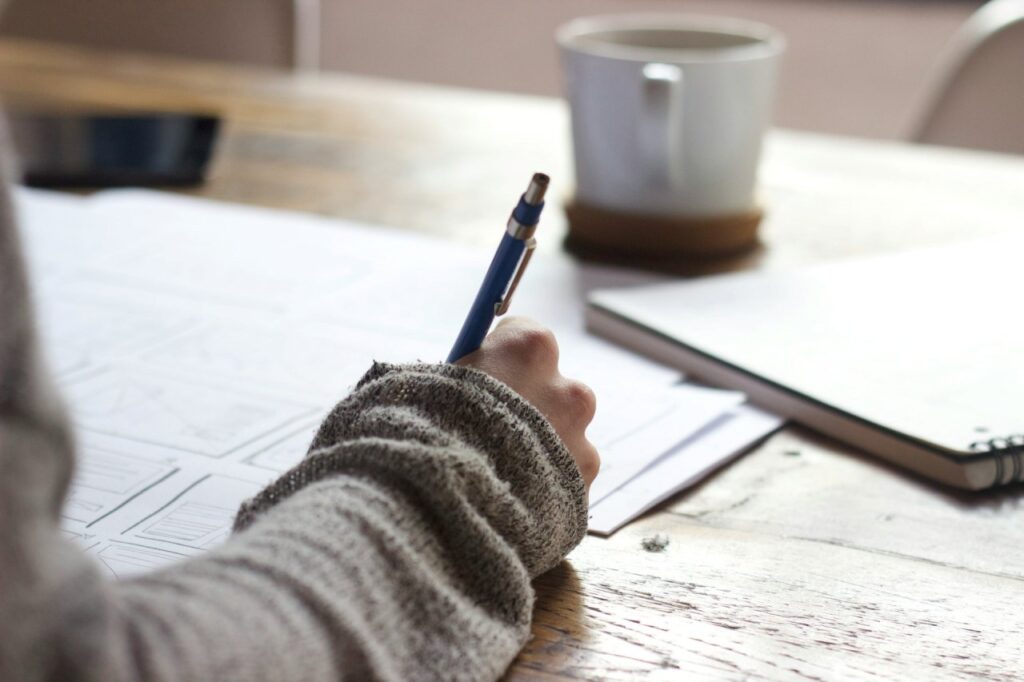 A student intensely focused on studying, writing notes with a pen on a table, preparing diligently to qualify for a scholarship.