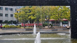 Busan International College fountain area, showcasing the campus environment with students relaxing near the water feature. A vibrant, dynamic space reflecting BIC's global academic opportunities and welcoming atmosphere.